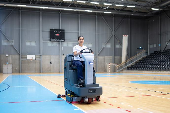 Cleaning machine scrubbing the floor inside a sports court at an entertainment venue.