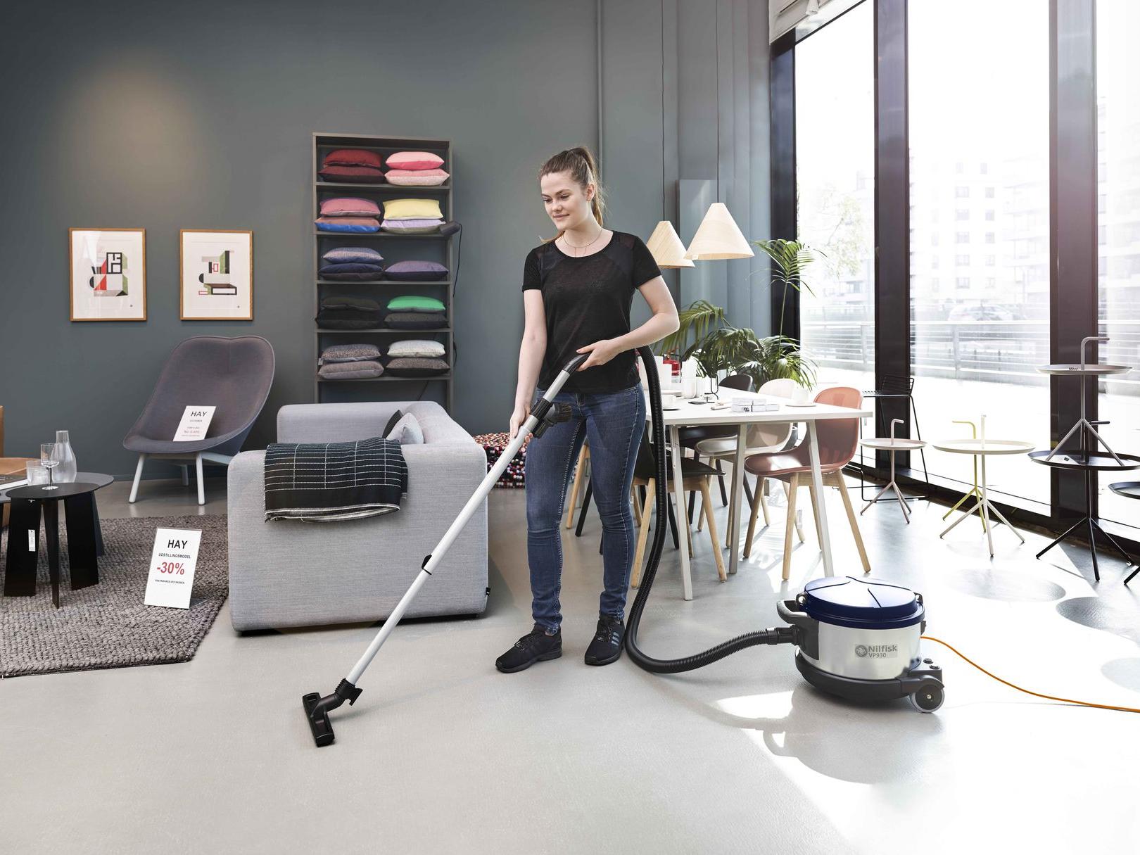 Worker cleaning floors inside a small retail store using commercial cleaning equipment.
