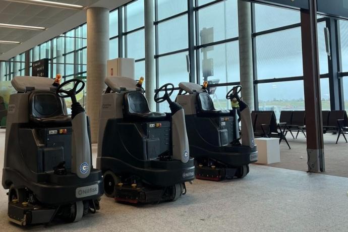 Ride-on scrubbers positioned inside an airport hangar or terminal for large-scale aviation floor maintenance